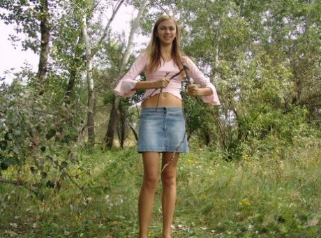 Young blonde exposes a bare shoulder while gathering twigs in the woods