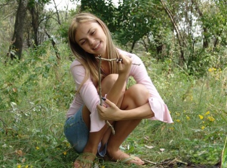 Young blonde exposes a bare shoulder while gathering twigs in the woods