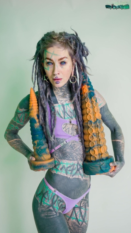 Heavily tattooed girl Anuskatzz holds a couple of taintacle toys in the nude