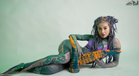 Heavily tattooed girl Anuskatzz holds a couple of taintacle toys in the nude
