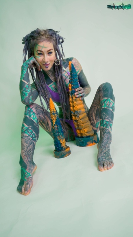 Heavily tattooed girl Anuskatzz holds a couple of taintacle toys in the nude
