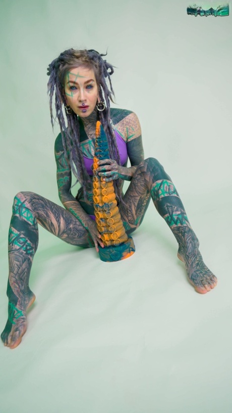 Heavily tattooed girl Anuskatzz holds a couple of taintacle toys in the nude