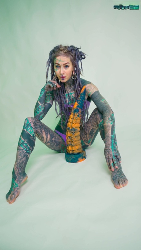 Heavily tattooed girl Anuskatzz holds a couple of taintacle toys in the nude
