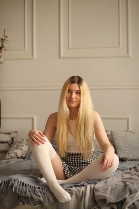 Young blonde beauty Suna slowly removes her clothing on top of her bed