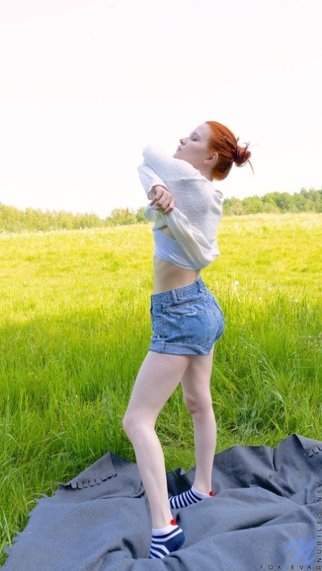 Pale redheaded teen Fox Eva gets naked on a blanket in a field