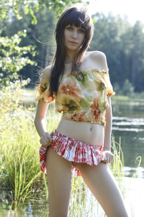 Beautiful teen Lena exposes her pert tits and bald cunt by the lake