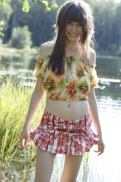 Beautiful teen Lena exposes her pert tits and bald cunt by the lake
