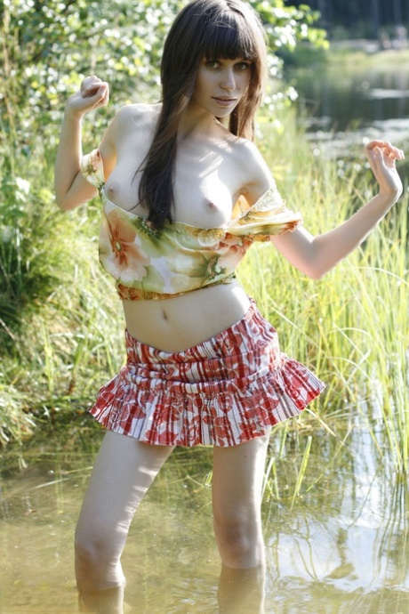 Beautiful teen Lena exposes her pert tits and bald cunt by the lake
